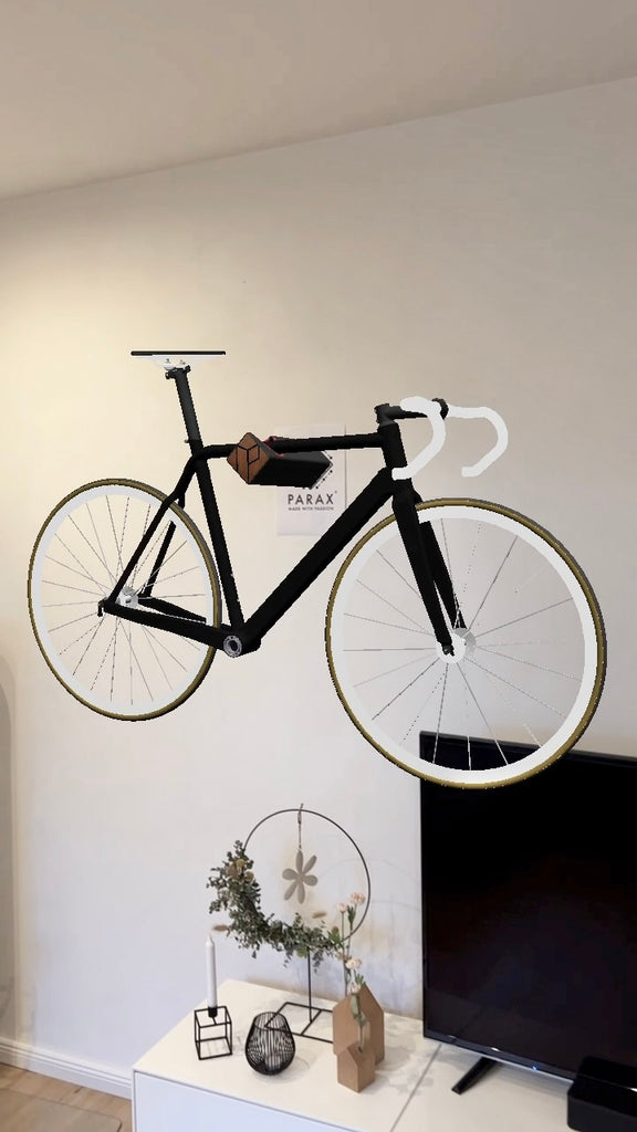 Schwarzes Augmented Reality Fahrrad auf schwarzer Fahrrad Wandhalterung D-RACK vor weißer Wand und schwarzem Fernseher